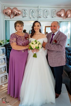 Wedding party poses together in front of decorative BRIDE letters in a blue-walled room.