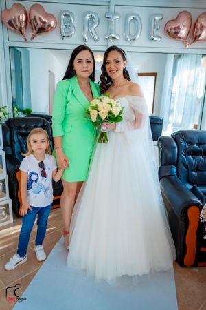 Wedding party in white dress and bright green attire pose together in a living room setting.