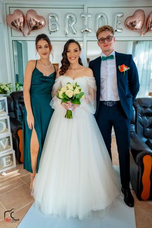 Wedding party members in formal attire gather for photos in front of decorative wall letters.