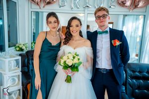 Wedding party gathered in a bright room with rose gold 'BRIDE' balloons and purple bridesmaid dresses.