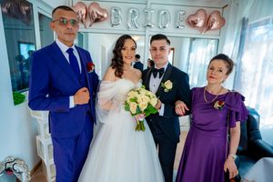 Wedding celebration with guests in purple dresses and formal suits under balloon decor.