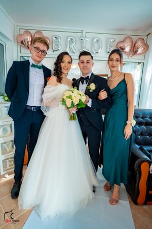 Formal wedding group photo with bride in white gown and guests in elegant attire.