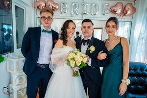 Wedding party members gathered in front of rose gold balloon letters in bright indoor setting.