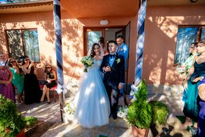 Wedding guests watch as couple poses on porch with terracotta walls and blue columns.