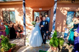 Guests gather to watch newlyweds on terracotta porch with blue columns.