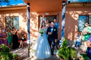 Festive outdoor wedding scene with guests gathered near coral-colored walls and blue pillars.