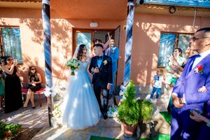 Outdoor wedding festivities with guests and decorations against a warm-colored building facade.