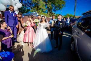 Wedding party celebrating outdoors with white balloons and guests in purple and pink attire.
