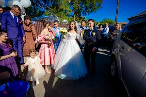 Outdoor wedding celebration with guests gathered around a car decorated with white balloons.
