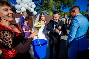 Wedding guests participate in a traditional celebration ritual with a blue bucket outdoors.