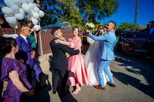 Wedding party members in purple and pink attire dancing and celebrating outdoors.