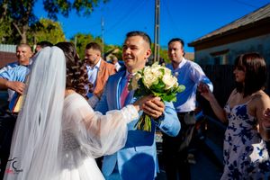 Outdoor wedding celebration with bouquet exchange and guests in bright formal attire.