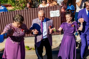 Guests in purple and blue formal attire dance at outdoor wedding celebration.