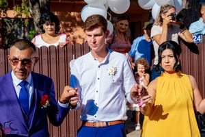 Wedding guests pose with white balloons against brown fence at outdoor celebration.