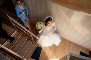 A wedding couple descends a modern wooden staircase with natural light streaming in from above.