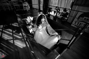 Black and white photo of a bride sitting on stairs with dramatic shadows.