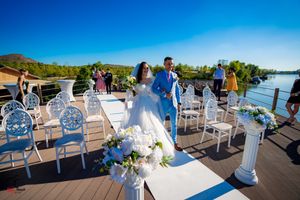 Outdoor waterfront wedding ceremony setup with white chairs and floral decorations on a wooden deck.