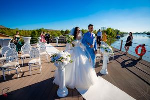 Wedding ceremony setup on a boat deck with white chairs and floral arrangements under bright blue skies.
