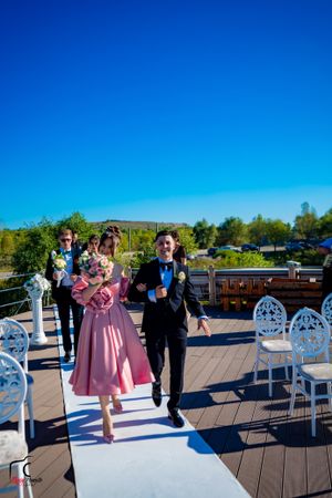Wedding attendants walking down a white aisle runner on an outdoor deck.