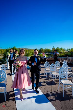 Wedding party members walking down an outdoor aisle under bright blue skies.