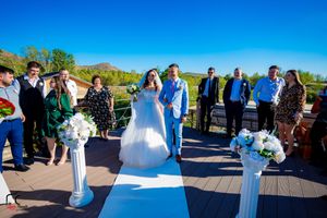 Outdoor wedding ceremony with guests gathered on a deck under bright blue skies.