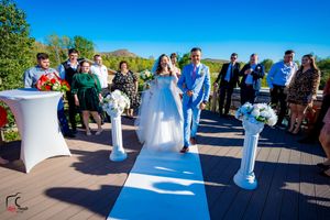 Outdoor deck wedding ceremony with white pedestals and blue runner against mountain backdrop.