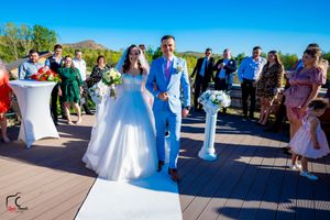Wedding ceremony on a sunny deck with white aisle runner and floral decorations.