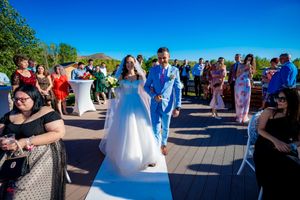 Wedding celebration on a deck overlooking water with guests in formal attire on a beautiful summer day.