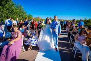 Wedding party and guests gather outdoors on a sunny day with bright blue skies and waterfront views.