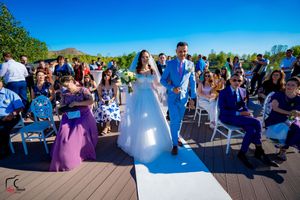 Wedding celebration on a waterfront deck with guests seated in rows under clear blue skies.
