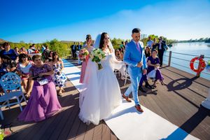 Wedding party poses for photos on a scenic waterfront deck during a sunny afternoon celebration.