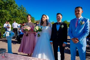 Wedding party in coordinated pastel colors poses together on a sunny deck by the water.