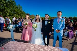 Formal wedding group photo with attendants in blue and purple standing on waterfront deck.