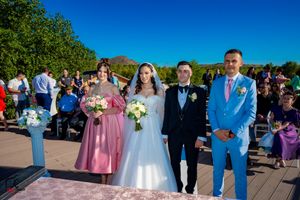 Wedding party gathered outdoors under bright blue sky with bridesmaids in pink dresses and groomsmen in suits.