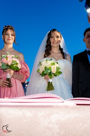 Wedding party members holding bouquets of pink and white roses against blue sky background.