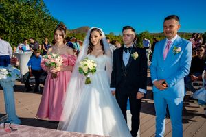 Wedding party poses outdoors with bridesmaids in pink dresses and groomsman in bright blue suit against mountain backdrop.