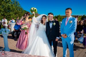 Wedding party celebrates on outdoor patio with mountains and blue sky in background.