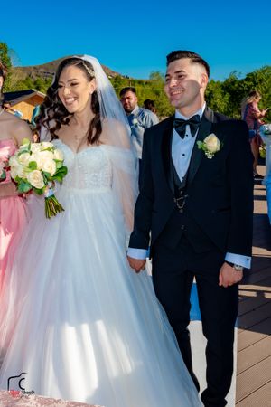 Elegant outdoor wedding ceremony with bride in white gown holding cream bouquet.