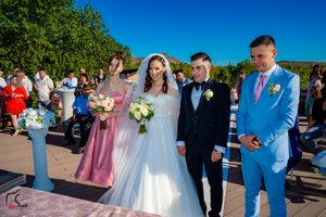 Outdoor wedding ceremony with bridal party in pink and blue attire against mountain backdrop.