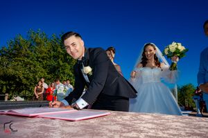Wedding couple signing marriage documents outdoors with blue sky backdrop.