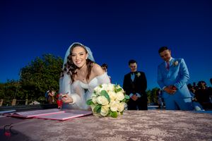 Wedding couple leaning over to sign documents during outdoor ceremony.