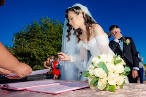Wedding guests sign documents outdoors against a bright blue sky background.