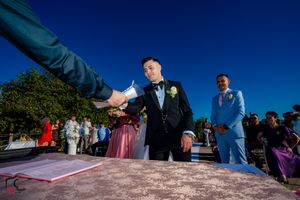 Outdoor wedding ceremony features document signing under bright blue skies.