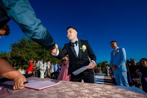 Wedding ceremony attendees gather on a wooden deck by a waterfront under bright blue skies.