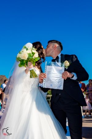 Wedding party in formal attire with white gowns and suits signing documents outdoors.