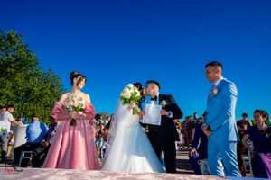 Outdoor wedding ceremony with white and pink decor against vibrant blue sky.