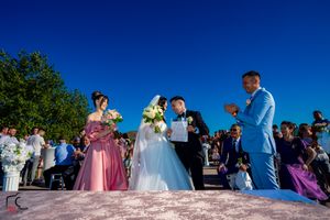Wedding celebration on waterfront deck with guests in formal attire and bright floral arrangements.