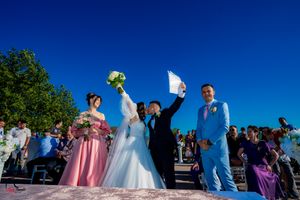 Wedding ceremony participants in formal wear gathered on sunny outdoor deck.
