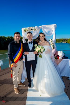 Formal wedding ceremony on wooden deck overlooking blue water with Romanian flag present.