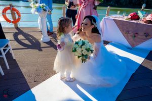 Wedding party poses on wooden deck by waterfront with white columns and floral decorations.